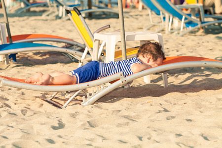Toddler dressed as a sailor lying on a sunbed on a beach. Photo with untraditional color rendering for artistic lookの写真素材