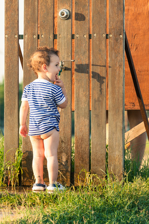 Toddler with sailor shirt eating his fingers and preparing to wash his feet after a visit to the beach. Photo with untraditional color rendering for artistic lookの写真素材