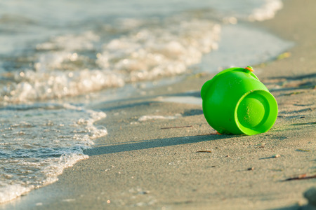 Toy bucket on a beach near the edge of the wavesの写真素材