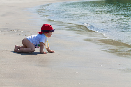 Baby crawling with determination on an untouched beach towards the waterの写真素材