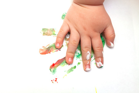 Close up of baby's hand covered with paint and a colorful imprint on white paperの写真素材