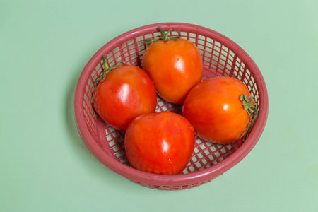 fresh four tomato in the red basket on the green tableの写真素材