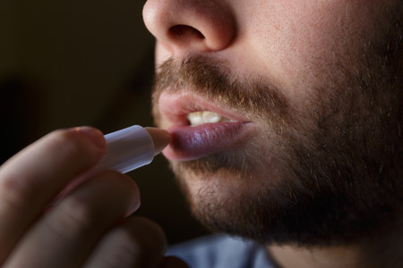 Young man with a beard repairing his damaged lips with moisturizerの写真素材