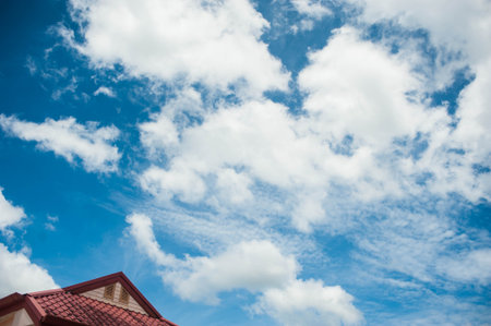 Blue sky with white clouds and red roof of house, nature backgroundの写真素材