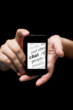 Hands Holding Smartphone, showing  Word Chat  printed , concept of communicating  online with mobile      
(on black background with very shallow depth of field)の写真素材