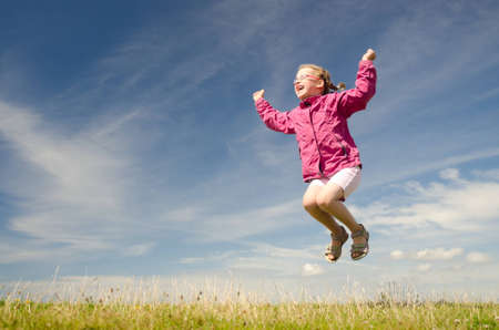 Happy little girl jumping in front of blue sky