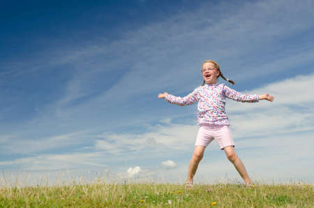 Happy little girl jumping in front of blue skyの写真素材