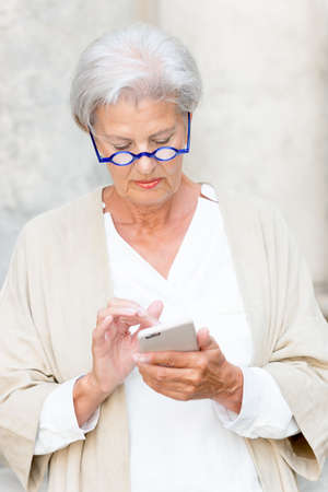 Senior woman with cell in front of a wallの写真素材