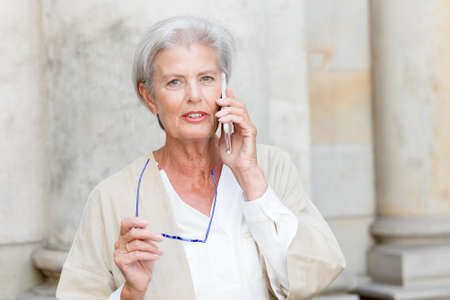Senior woman with cell in front of a wallの写真素材