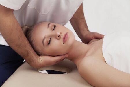 Osteopath makes head and neck massage to a girl on a white backgroundの写真素材
