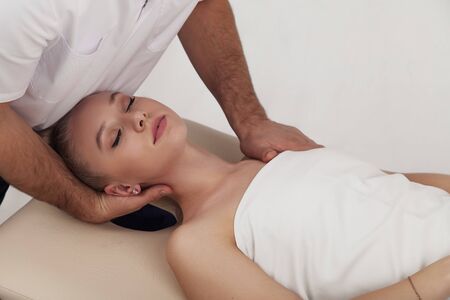 Osteopath makes head and neck massage to a girl on a white backgroundの写真素材