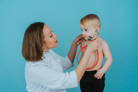 Woman doctor listens with a stethoscope to the lungs of a little boyの写真素材