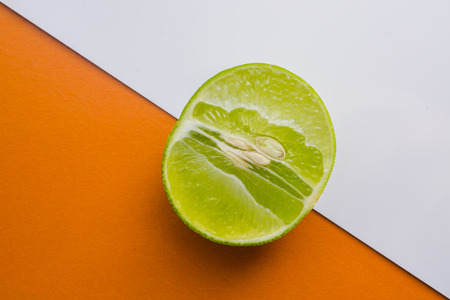 top view slice of fresh lime half on the orange and white background.の写真素材