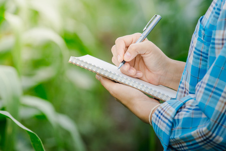 Woman's hand take notes with a pen on a notebook in agriculture garden.の写真素材