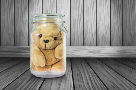 Teddy bear in a glass jar on gray wood backgroundの写真素材
