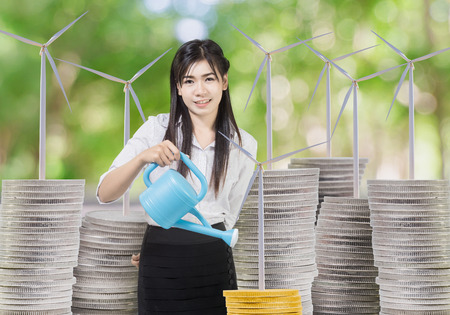 Young businesswoman watering wind turbineon coins with can. concept Wind energy investmentの写真素材