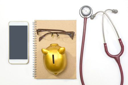 Top view of stethoscope, mobile phone, gold piggy bank, glasses and brown notebook on white background, flat lay.の写真素材