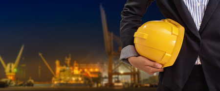 person holding yellow helmet for workers security on industrial port background at nightの写真素材