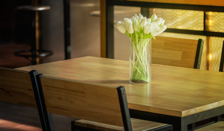 White tulips in a vase are placed on a wooden table.