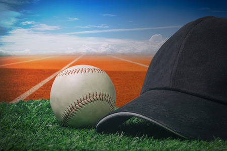 Black cap and a baseball on a green grass with a red running track and blue sky.