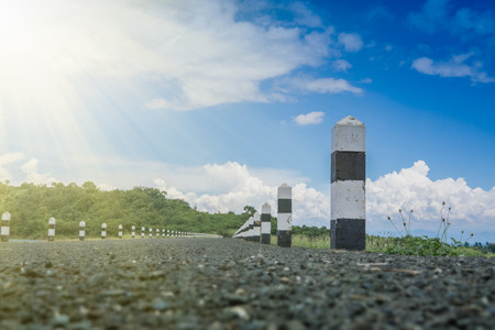 Black and white stones beside road with blue sky and sunbeam. kilometer stone