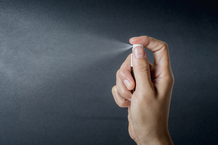 close up hand hold small spray bottle and spraying on dark background.の写真素材