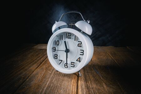 white retro alarm clock on wood table with dark background