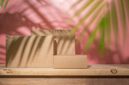 Brown podium stage from paper box on wooden table on pink background with shadows of palm leaf for use show productの写真素材