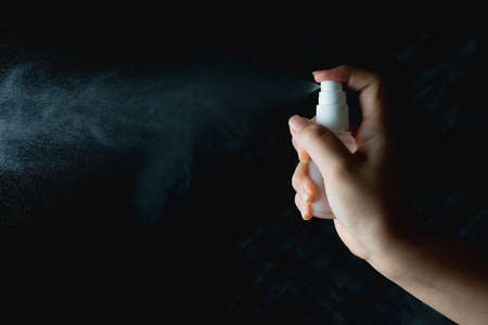 close up woman handing small spray bottle and spraying on dark backgroundの写真素材