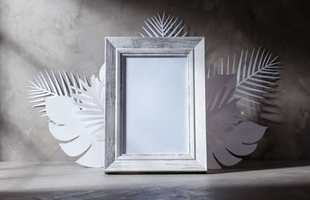 empty wooden white old style picture frame decorate with white paper cut style elements of leaf on concrete background with shadow window, copy spaceの写真素材