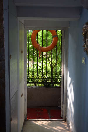 Orange lifebuoy hanging from a metal door of an old houseの写真素材