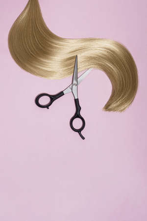 Woman cutting hair. Smooth light strand of hair and scissors. On a pink background, top view.の写真素材