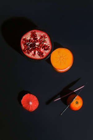Flat lay layout with pomegranate, orange, persimmon, grapefruit fruit on black background. Minimal concept with sharp shadows. Trendy social mockup.の写真素材