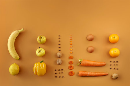 Creative layout with bananas, nuts, dried apricots, oranges, apples, carrots, peppers and lemon in yellow and orange colors. On a light brown background, top view. Vitamins and healthy food concept.の写真素材