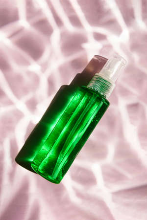 Gel or serum in a green bottle with sun shadow. On a pink background with reflections of water. View from above.の写真素材
