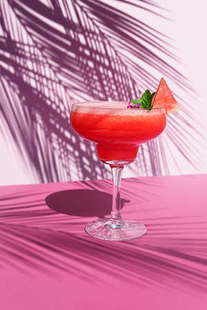 Watermelon cocktail on the table with sun shadows. On a pink background with palm leaves, front view.の写真素材