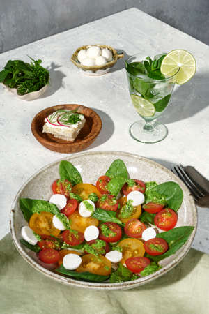 Composition with salad and cocktail. Composition with a salad made of tomatoes, spinach, basil, cheese. On the background of a concrete table.の写真素材