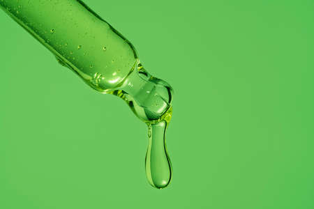 A drop of serum from a pipette. On a bright green background.の写真素材