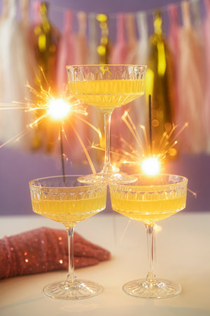 New Year Card Design with three glass of champagne and sparkler. On a purple background with colored paper garland.の写真素材