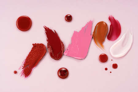 Smears of different colors are made with various cosmetic products. On a pink background. Texture of...