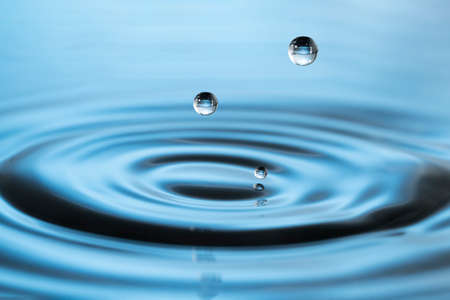 Drops of water falling on smooth wet surface. Blue blurred background.の写真素材