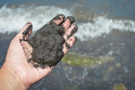 The hand holds black volcanic sand by the beach of the volcanic caldera lake Laguna de Apoyo in the highlands near Masaya, Nicaragua. Central Americaの写真素材