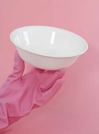 hand with glove on holding a white bowl, pink background