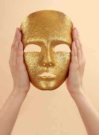 woman hands holding a gold mask, beige backgroundの写真素材