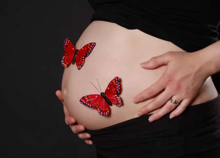 closeup on pregnant woman belly with fake red butterfliesの写真素材