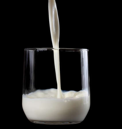 pouring milk in a small glass, black backgroundの写真素材