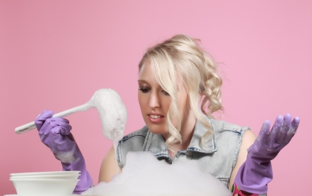 cute young blond woman washing dishes, pink backgroundの写真素材