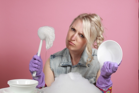 cute young blond woman washing dishes, pink backgroundの写真素材