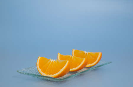 Three pieces of fresh oranges on a plate, blue backgroundの写真素材
