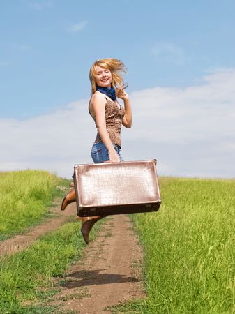attractive young blond woman with an old leathern suitcase jumping outdoor on the roadの写真素材